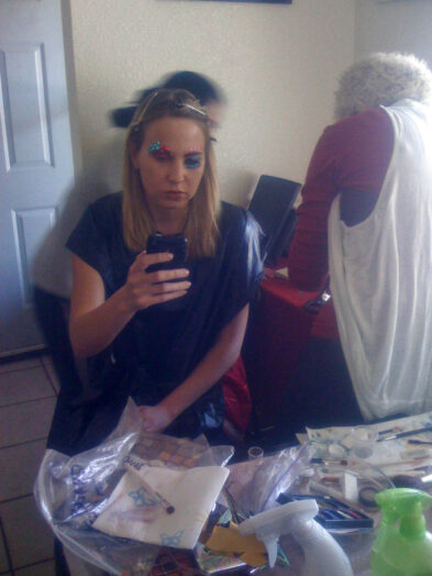 Model Anne checks her phone while wearing colorful Octopus Project makeup as preparations continue around her.