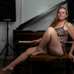 Portrait of Swisha Sweet reclining on a piano bench while wearing a leopard-print lounge set in a studio setting.