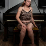 Portrait of Swisha Sweet seated on a piano bench wearing a leopard-print lounge set in front of a grand piano.