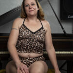 Close-up portrait of Swisha Sweet seated on a piano bench wearing a leopard-print lounge set in a studio.