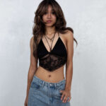 Portrait of Dallas M. smiling while wearing a black lace halter top and rhinestone-studded jeans against a white studio wall.