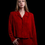 Fashion portrait of TamLynn Link wearing a red textured blouse and matching red pants against a black studio background.