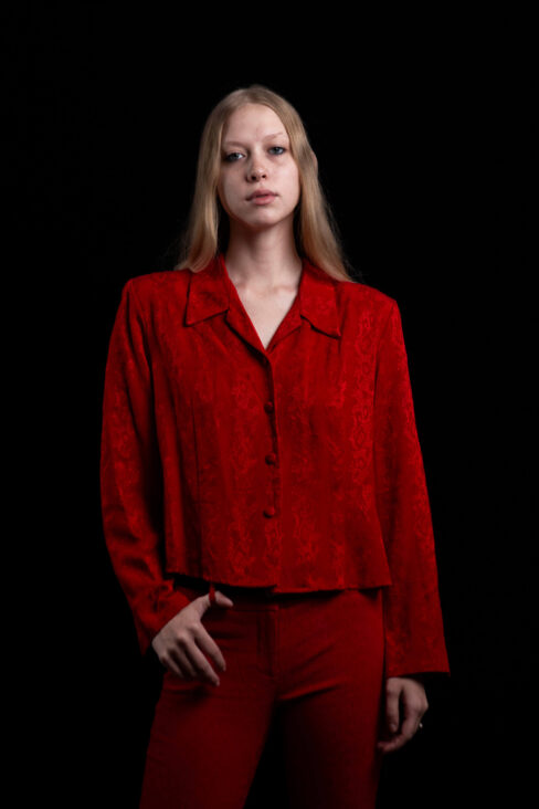 Fashion portrait of TamLynn Link wearing a red textured blouse and matching red pants against a black studio background.