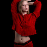 Studio portrait of TamLynn Link in a red outfit with arms raised above her head against a black background.