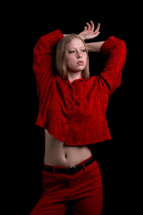 Studio portrait of TamLynn Link in a red outfit with arms raised above her head against a black background.
