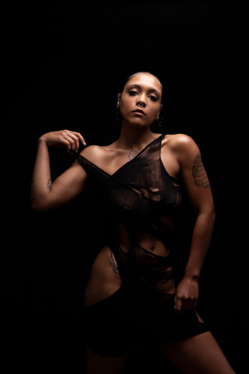 Artistic studio portrait of Vinny Young posing against a black background while wearing a distressed black garment.
