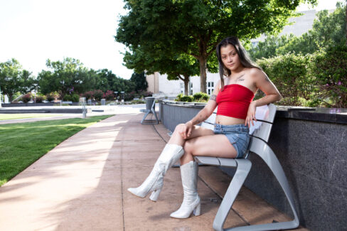 Augustine Amasaman seated on a modern bench in downtown Oklahoma City wearing sparkling white boots and casual summer fashion.