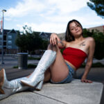 Model Augustine Amasaman posing on a concrete bench in downtown Oklahoma City wearing a red tube top, denim shorts, and sparkling white boots.