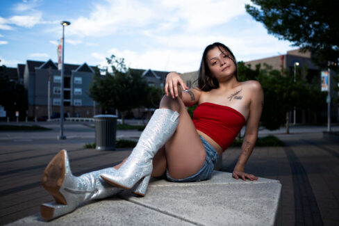 Model Augustine Amasaman posing on a concrete bench in downtown Oklahoma City wearing a red tube top, denim shorts, and sparkling white boots.