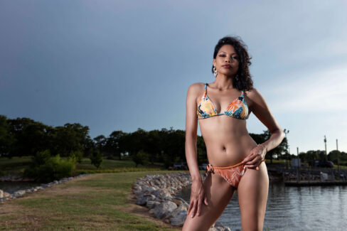 Lemon Drop posing in a floral bikini beside a lakeside shoreline under dramatic storm clouds.