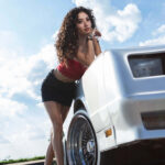 Jas leaning against the front fender of a silver Monte Carlo beneath a bright summer sky.