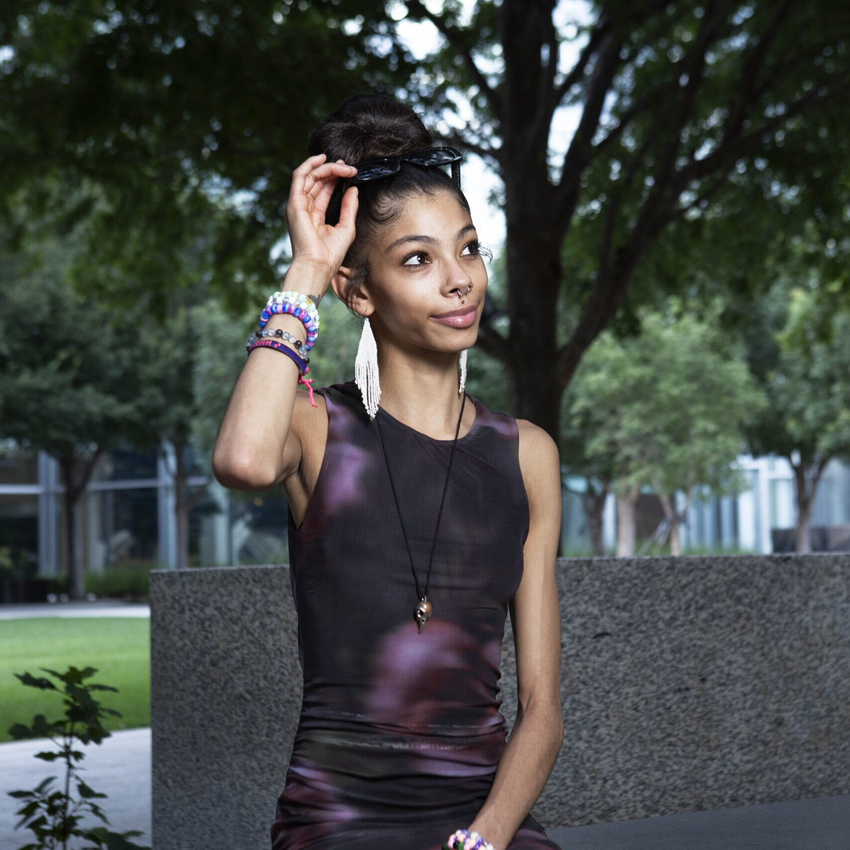 Bratzdoll seated on a bench outside Devon Tower adjusting her sunglasses during a downtown Oklahoma City portrait session.