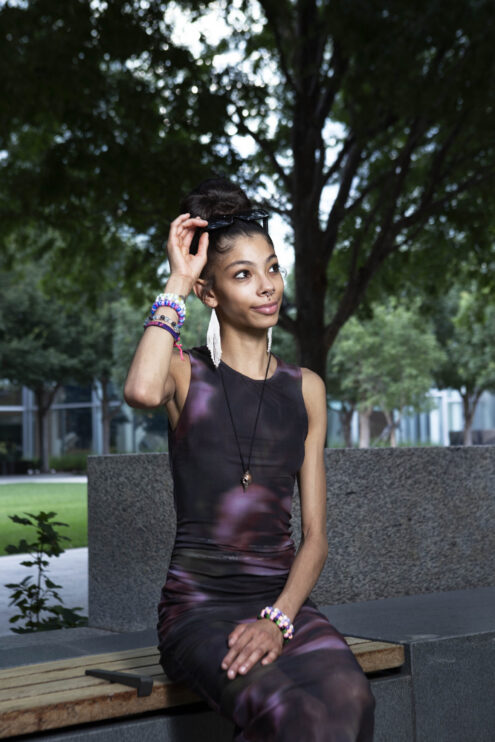Bratzdoll seated on a bench outside Devon Tower adjusting her sunglasses during a downtown Oklahoma City portrait session.