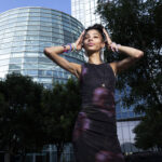 Bratzdoll posing in front of Devon Tower with modern glass architecture in downtown Oklahoma City.