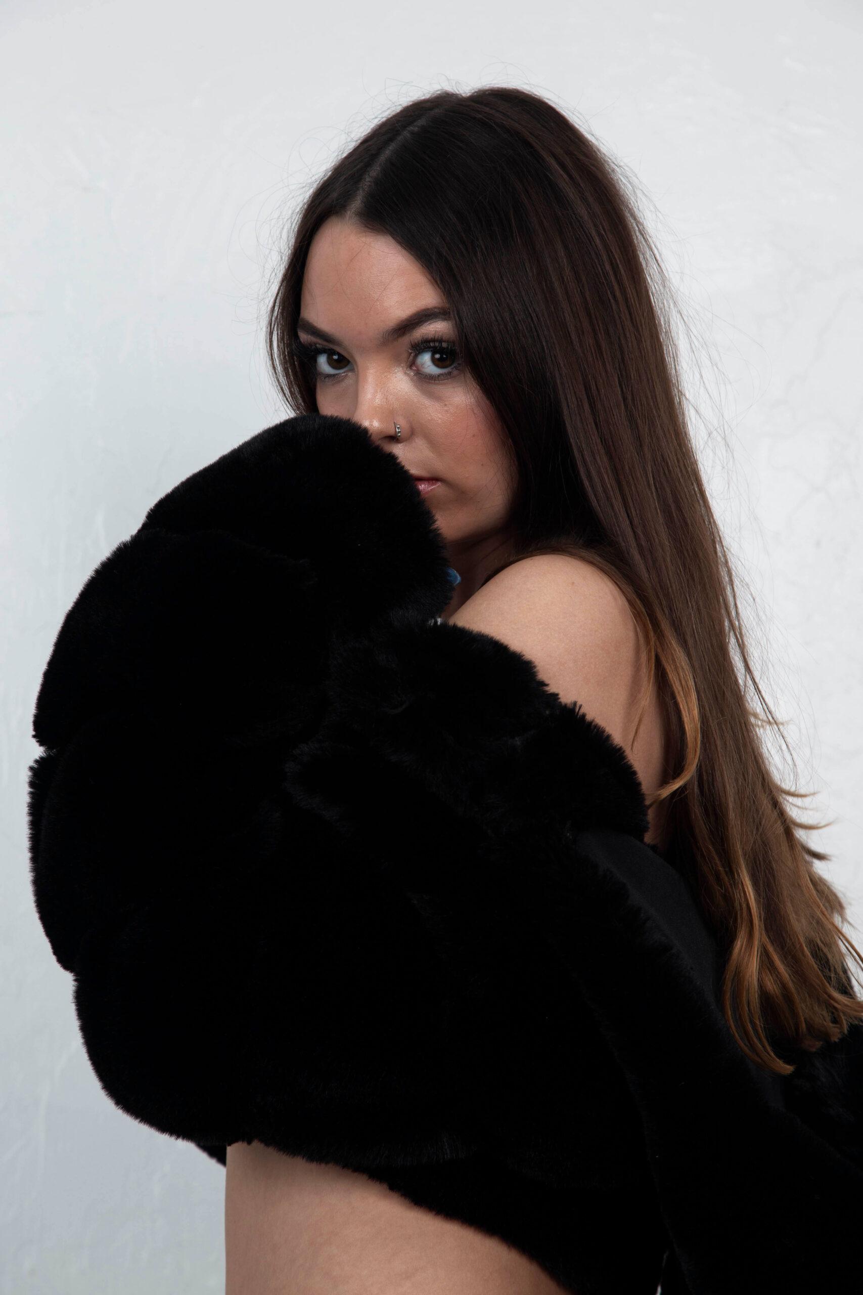 Shordy Kyy poses in a black faux-fur garment against a white studio background, looking directly toward the camera.