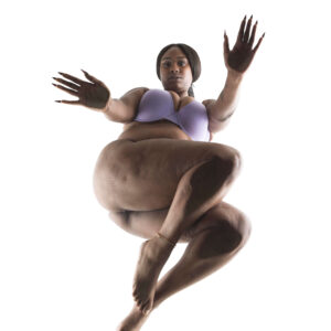 2Litt Modeling poses in lavender lingerie with her legs crossed and both hands reaching toward the camera against a bright white background.
