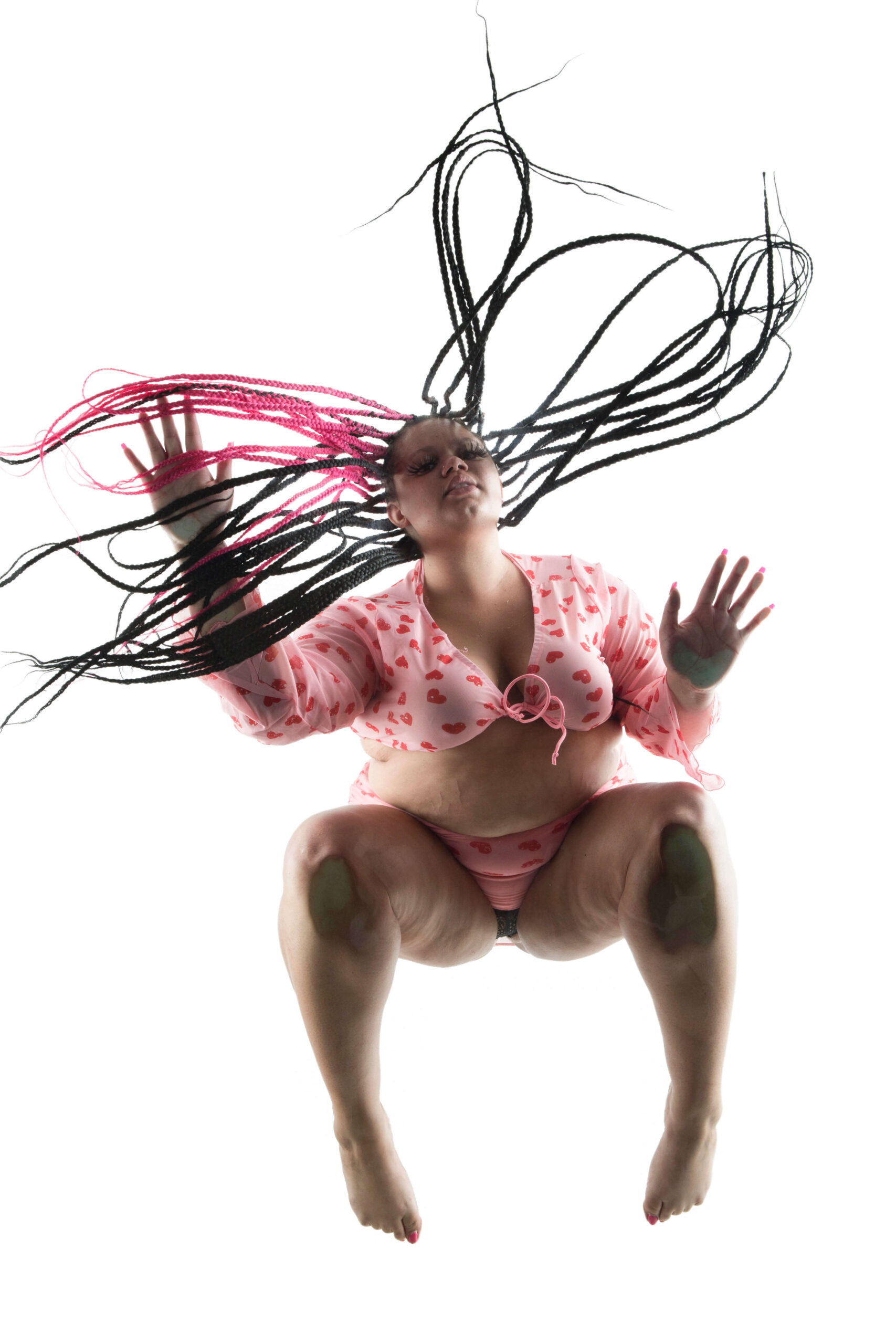Kylee the Model poses above a glass platform in a pink heart-patterned outfit, with long black and pink braids spreading dramatically across the frame.