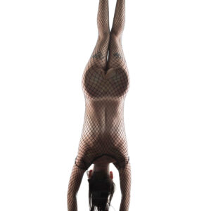 Nikki Haze hangs upside down against a bright white background, her body enclosed in black fishnet material with her arms extending downward.