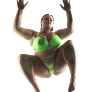 Kylee the Model poses on a transparent glass platform in neon green lace lingerie, photographed from directly below against a bright white background.