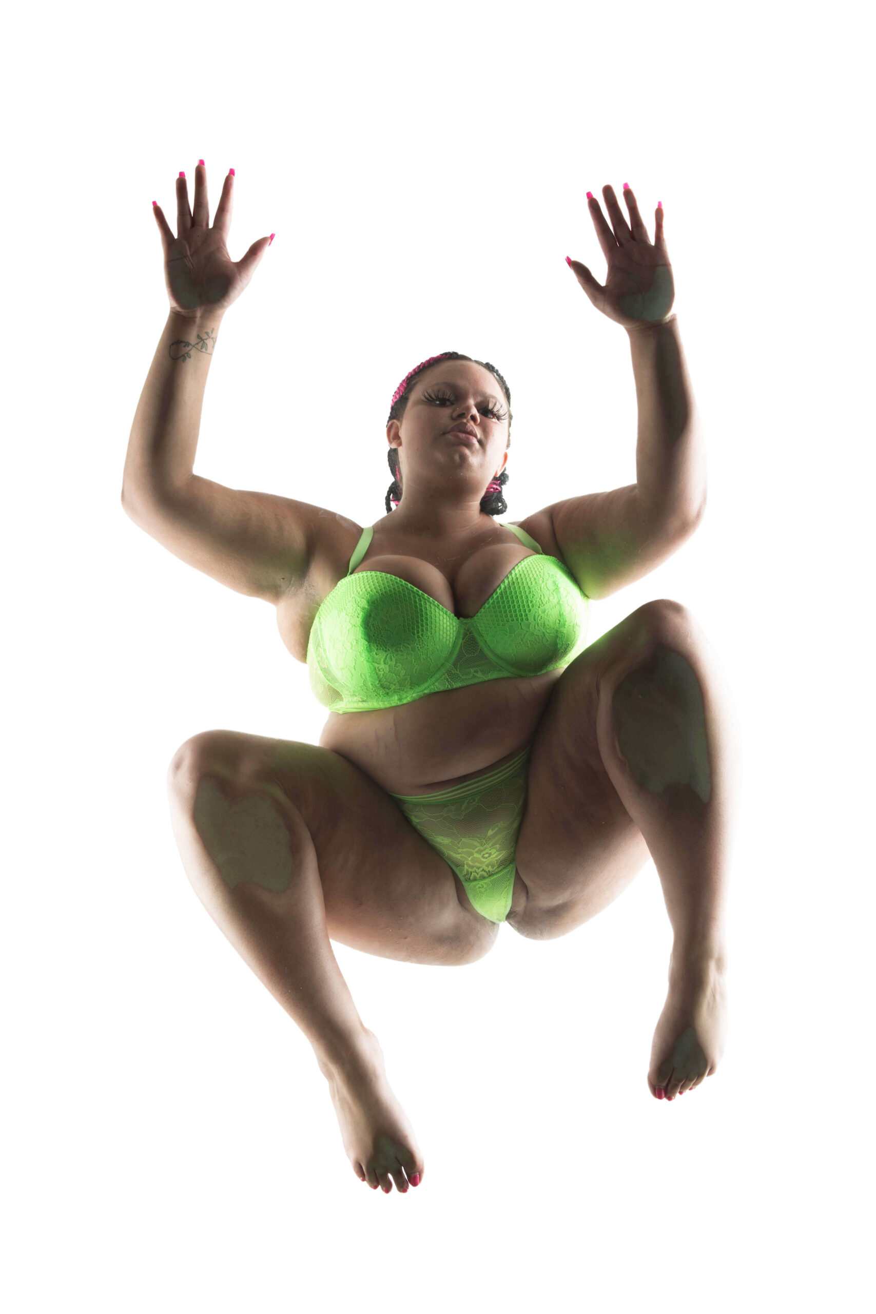 Kylee the Model poses on a transparent glass platform in neon green lace lingerie, photographed from directly below against a bright white background.