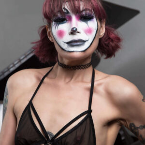 Kody Kathleen poses in a close-up portrait wearing dramatic black, white, and pink clown-inspired makeup, sheer black lingerie, a black choker, and her hair styled in pigtails.