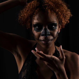 Saturn poses against a black background wearing dramatic black skull-inspired face makeup and black lace, framed by expressive hand gestures.