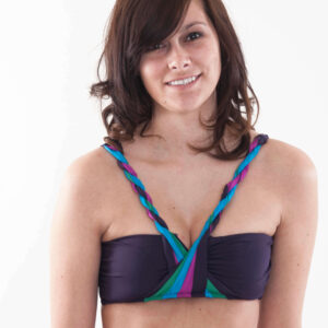 Model Marisol L smiles at the camera while wearing a colorful purple, turquoise, green, and pink bikini top against a white studio background.