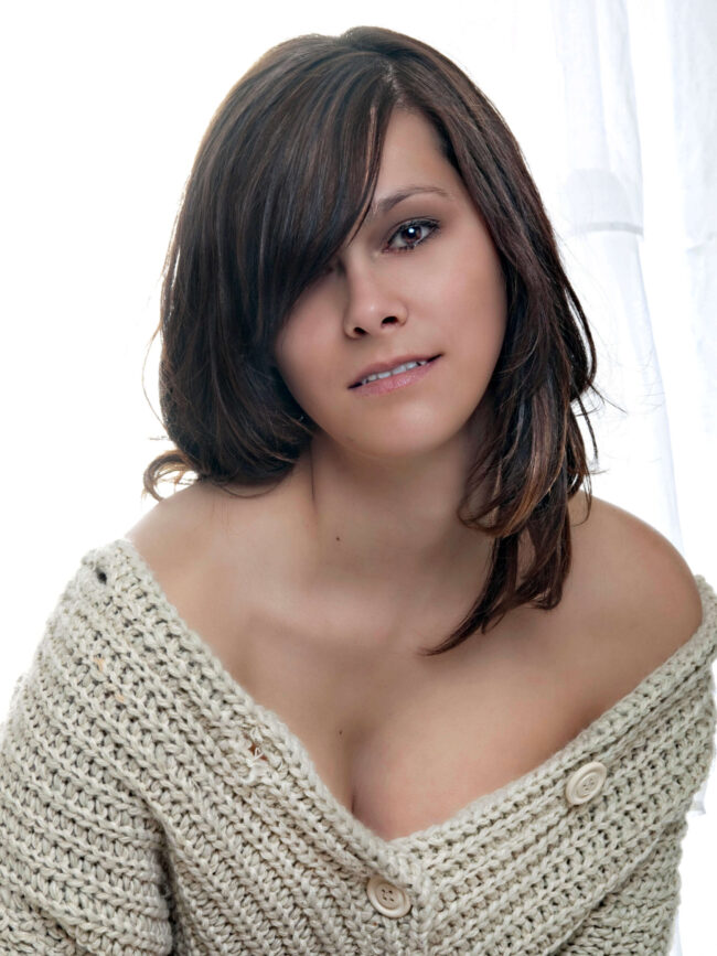 Marisol L Close-up portrait of model Marisol L wearing a cream knit sweater draped off her shoulders, photographed against a bright white backlit background.