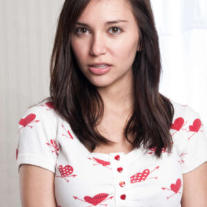 Model Kylie Hunter poses for a close-up portrait wearing a white top patterned with red hearts and arrows during an indoor fashion photo shoot.