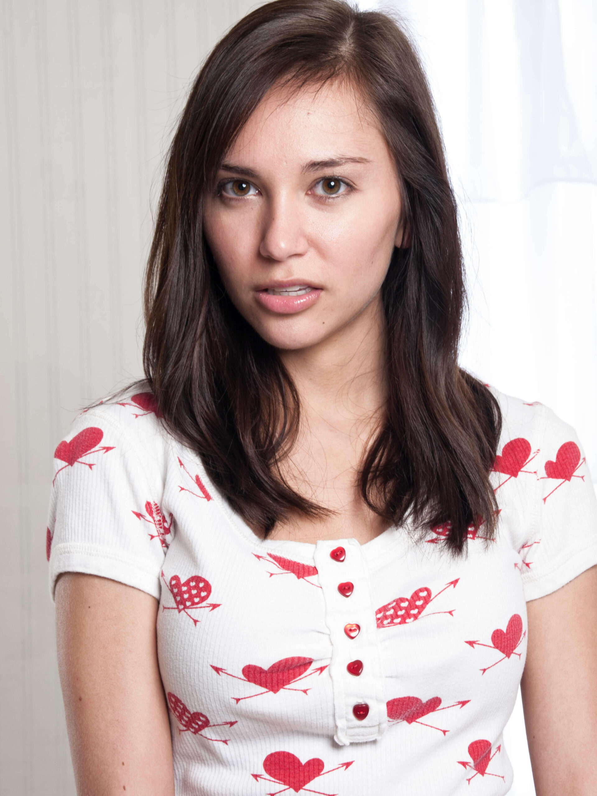 Model Kylie Hunter poses for a close-up portrait wearing a white top patterned with red hearts and arrows during an indoor fashion photo shoot.