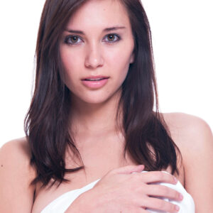 Model Kylie Hunter poses for a close-up studio portrait with long brunette hair, holding white fabric against a bright white background.
