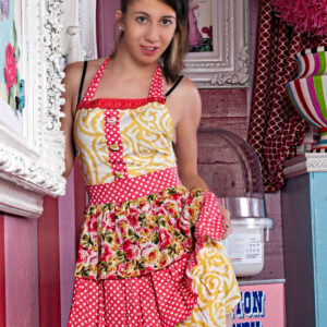 Tiffany poses in a colorful interior wearing a vibrant retro-style apron featuring red polka dots, floral fabric, and yellow patterned panels.
