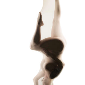 Felicity Sparks appears suspended upside down against a luminous white background, her body gracefully contorted into a dramatic, sculptural pose. Sheer fabric softens her silhouette, while extended legs, expressive hands, and delicate shadows create an ethereal composition emphasizing movement and the beauty of the human form.