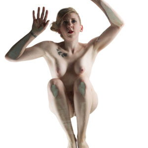 Hippy Researcher poses nude with both arms raised and knees drawn upward against a bright white background in a striking high-key fine art nude portrait.