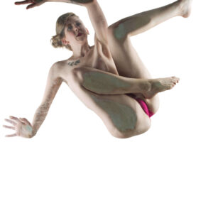 Hippy Researcher poses in a dramatic, suspended position with arms outstretched and legs extended at contrasting angles against a brilliant white background in a high-key fine art nude photograph.