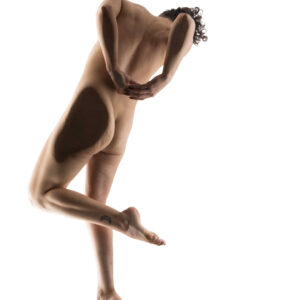 Fine art nude photograph of Julia Wagner captured from behind in a graceful, suspended pose against a bright white background, emphasizing sculptural curves and artistic movement.