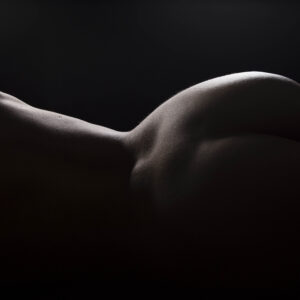 Fine art nude silhouette of Julia Wagner reclining against a black background, with dramatic rim lighting highlighting the elegant curves of her body in a low-key studio photograph.